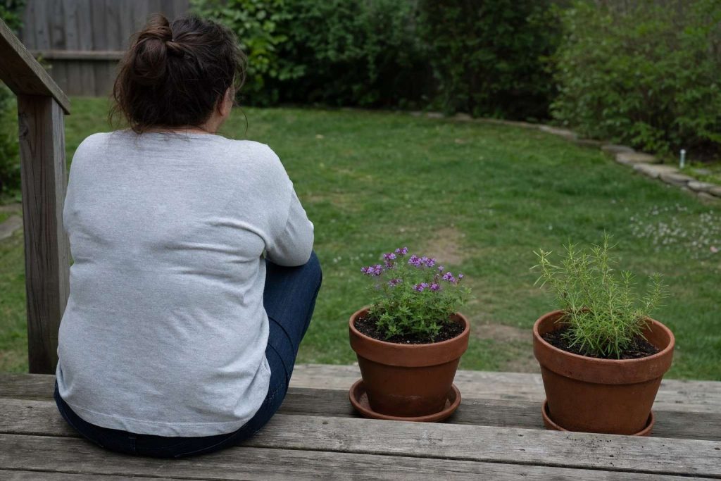 a person sitting on porch steps beside a couple of potted plants, not working, just looking at them