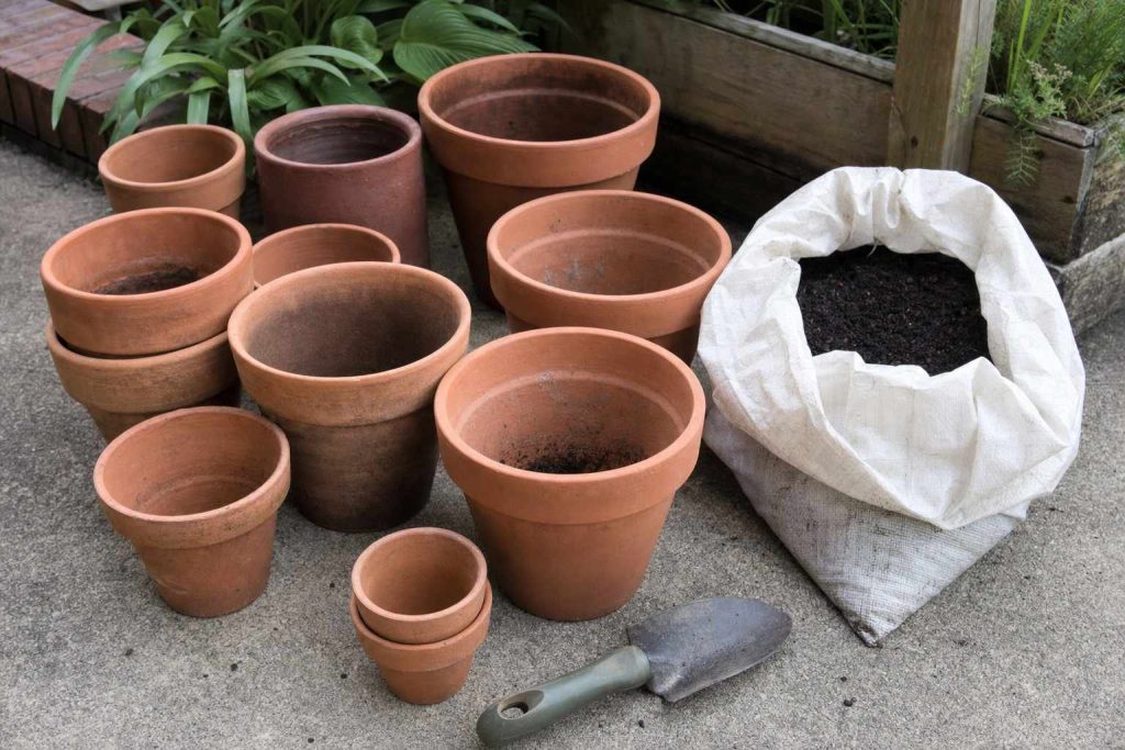 empty terracotta pots of different sizes grouped on a patio floor beside an open bag of potting mix