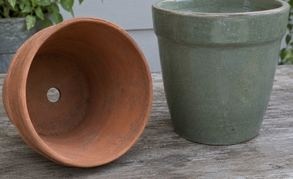 a terracotta pot tipped on its side showing an open drainage hole next to a glazed pot with a solid base